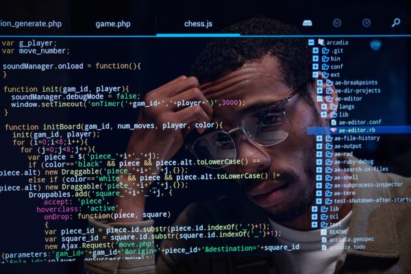 Analyzing Code on Multiple Screens with Focus Man focused on analyzing code displayed on multiple screens with reflections in glasses. Lines of code visible in foreground showing complex programming process