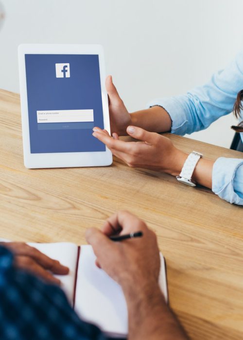 partial view of businesswoman with tablet with facebook logo and colleague with notebook taking part partial view of businesswoman with tablet with facebook logo and colleague with notebook taking part